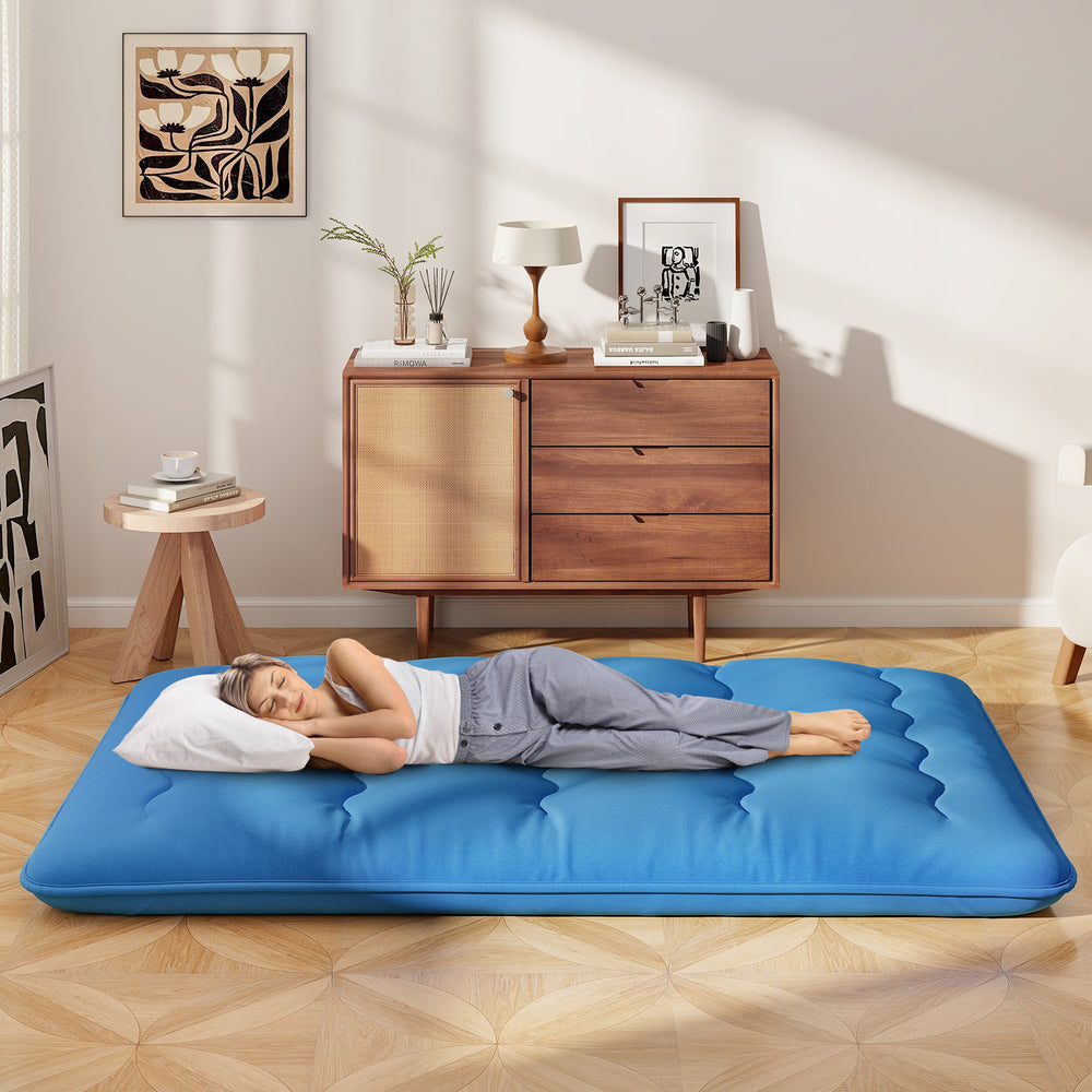 Blue foldable futon mattress with washable cover, shown in a cozy indoor setting, ideal for camping or home use.