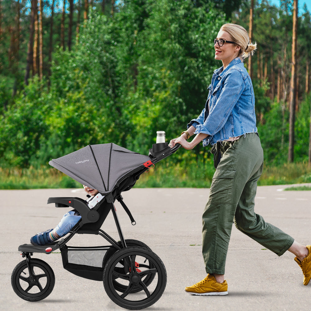 Jogging stroller in gray being pushed by a parent, featuring a spacious storage bag and adjustable canopy for.