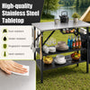 Foldable outdoor cook station with stainless steel tabletop, removable shelves, and trash bag holder for camping convenience.