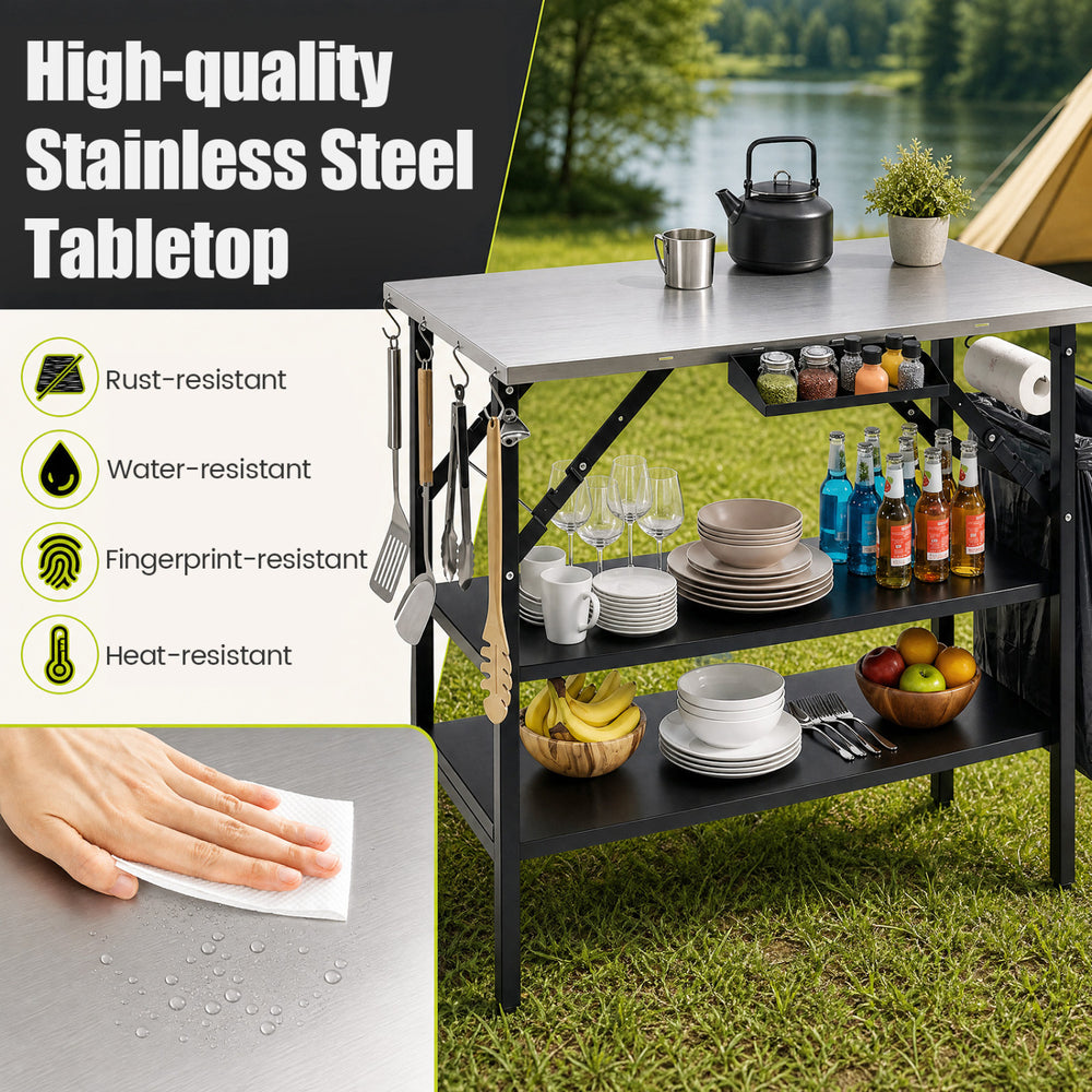Foldable outdoor cook station with stainless steel tabletop, removable shelves, and trash bag holder for camping convenience.