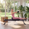 Foldable Pilates reformer machine in black, used for home workouts, featuring a woman performing exercises indoors.