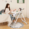 Folding gray baby dining high chair with adjustable height and recline, shown in use at a dining table.