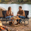 Folding camping chairs with side table and cup holder, perfect for outdoor picnics and fishing, shown by a lakeside.