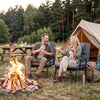 Folding camping cot in gray, shown as a chaise lounge chair by a campfire, featuring a removable cushion and sturdy.