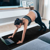 Folding gymnastics mat in black with a woman practicing yoga, featuring a sweatproof PU leather cover and carry handles.