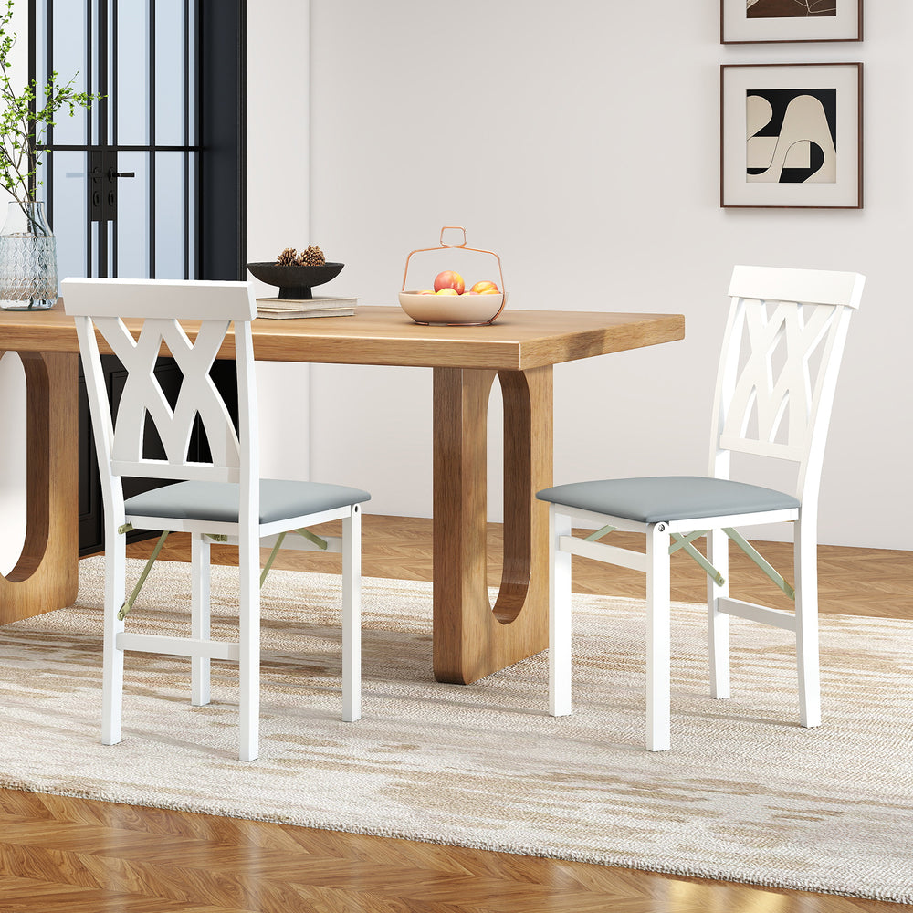 White folding wooden dining chairs with faux leather upholstery, featuring X-shaped backs, ideal for small spaces.