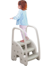 Toddler using a gray 3-step stool with safety handles and non-slip pedals for kitchen tasks. Ideal for ages 1+.