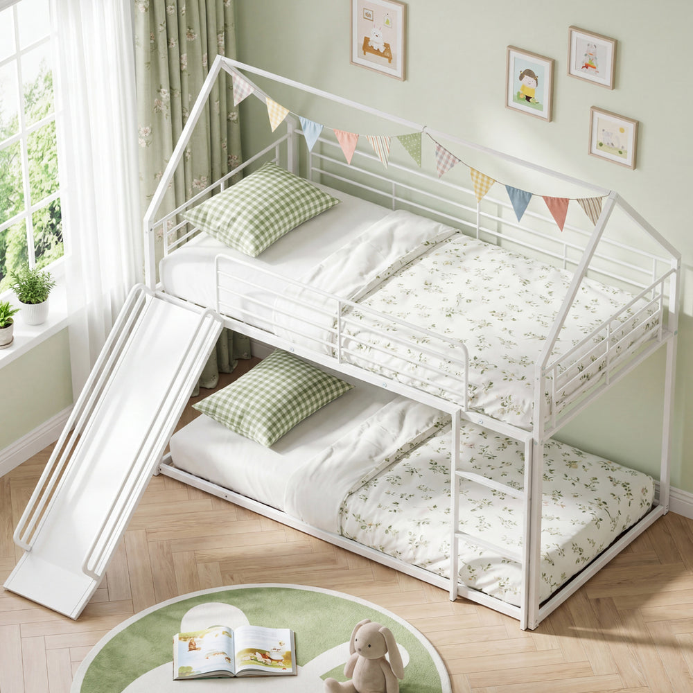 House-shaped white metal twin over twin low bunk bed with slide and floral bedding, perfect for children's rooms.