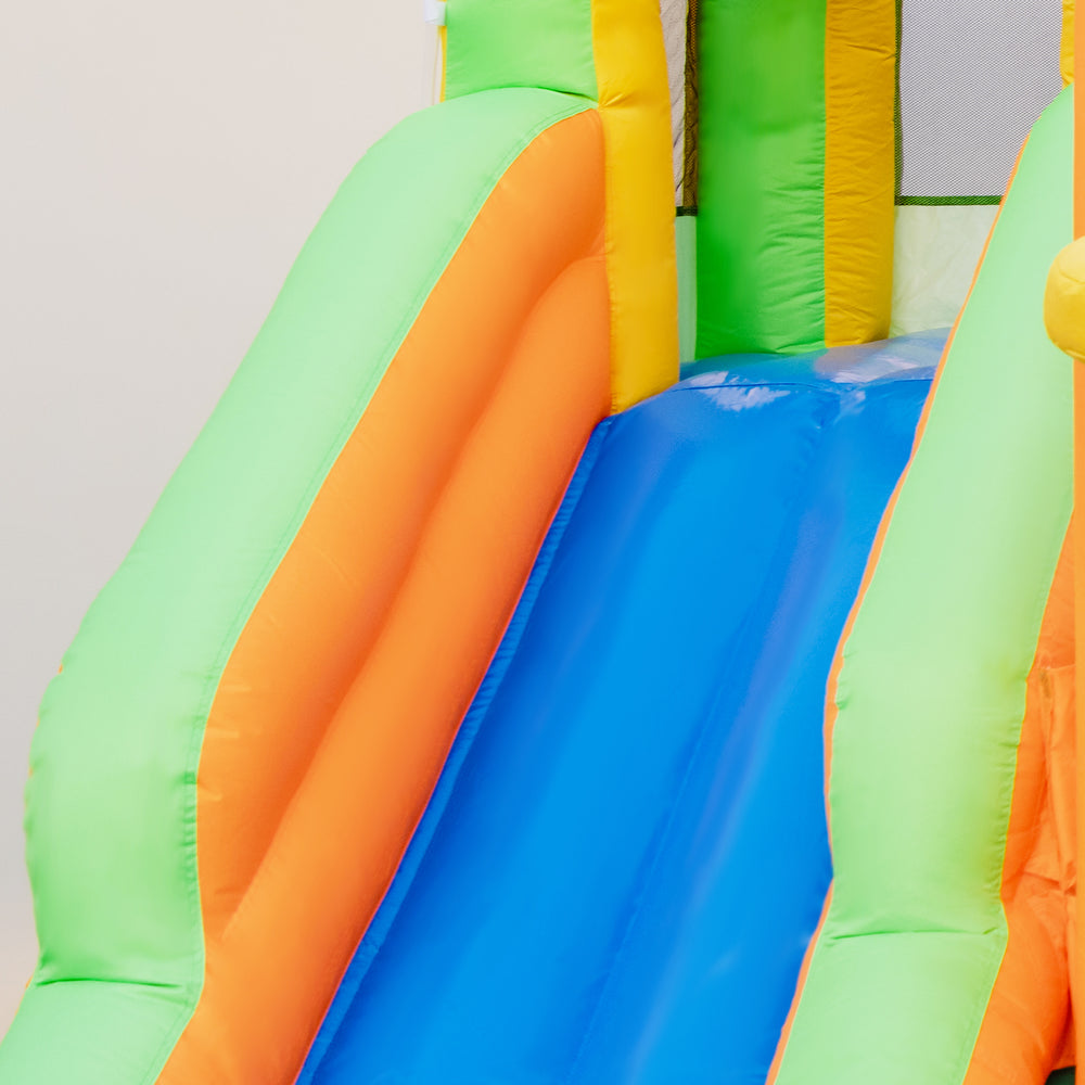 Brightly colored inflatable water slide with blue surface, featuring two slides and a climbing wall for kids' summer.