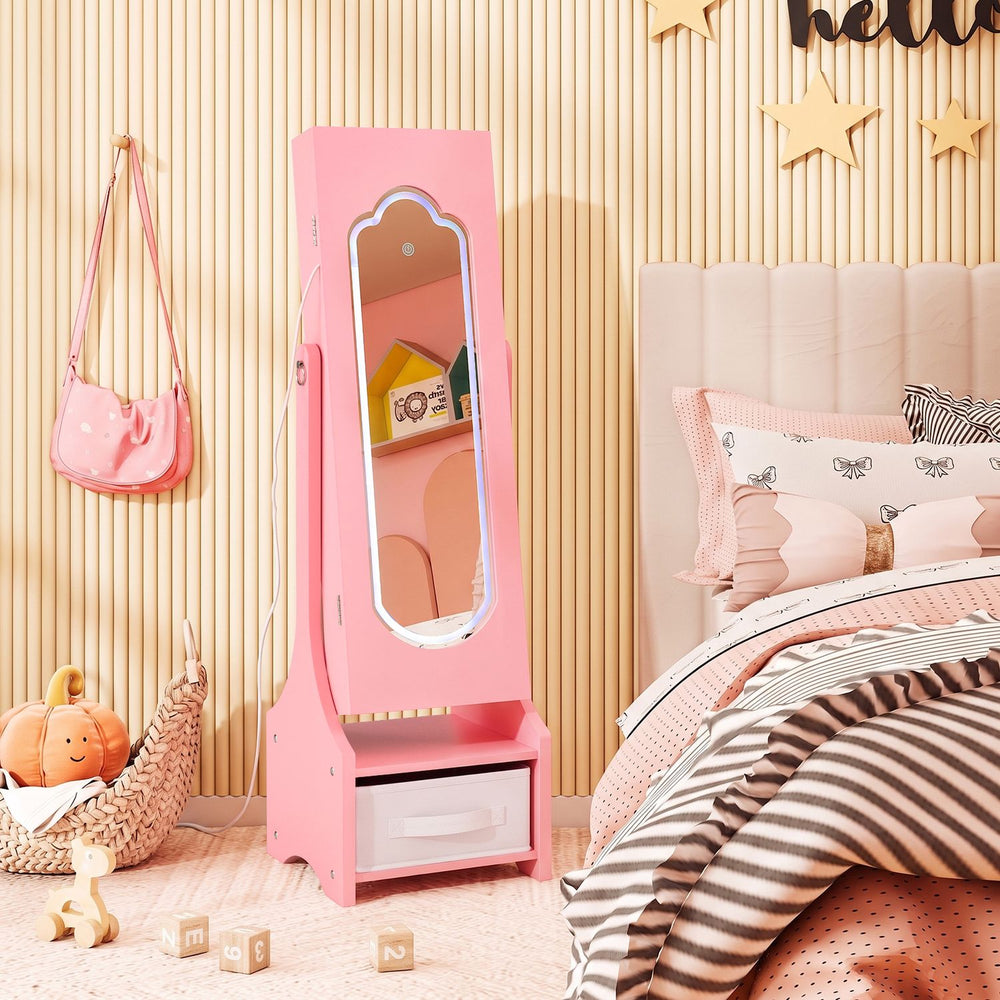 Pink kids jewelry armoire with full-length mirror and LED light stands beside a bed in a decorated child’s bedroom.
