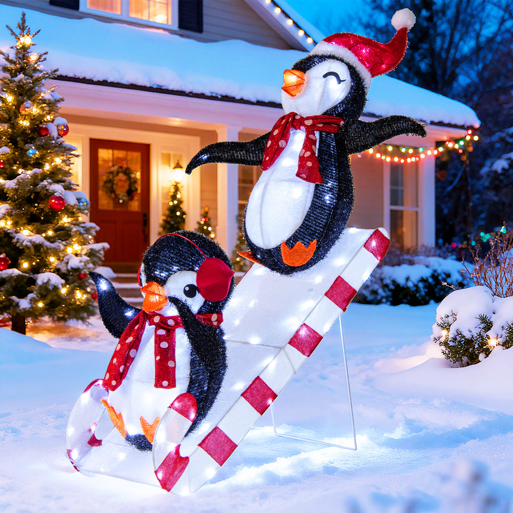3D lighted Christmas decoration featuring two penguins on a slide, adorned with red hats and scarves, for festive.