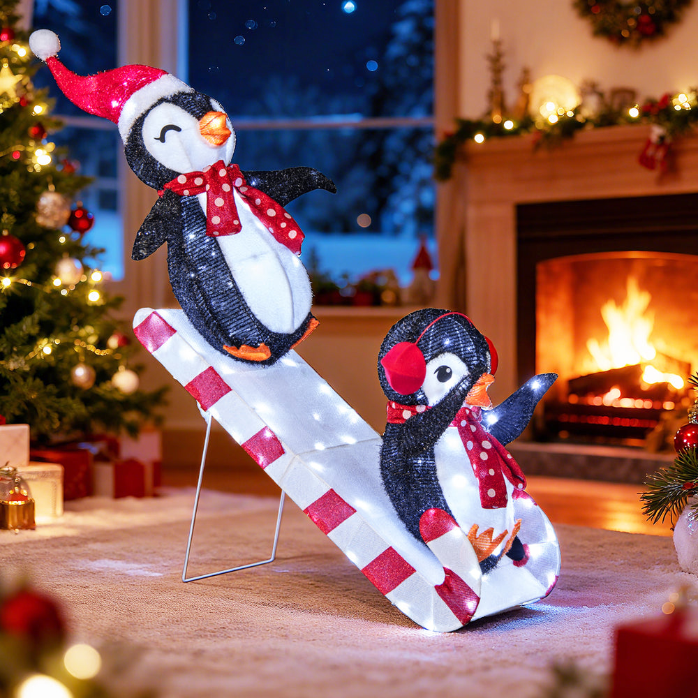 3D lighted Christmas decoration featuring two penguins on a slide, adorned with red hats and scarves, ideal for festive.