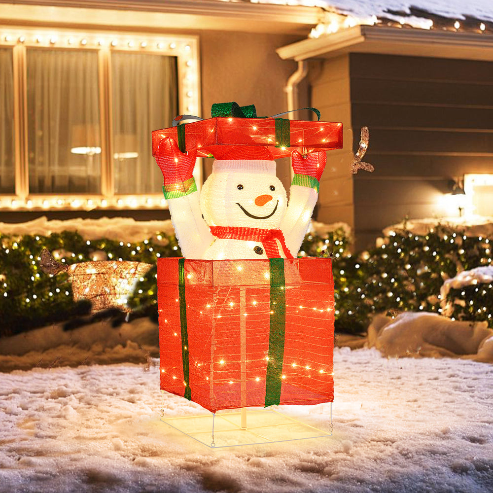 Lighted snowman wearing a red scarf in a large gift box, decorated with 100 warm LED lights for festive outdoor display.