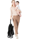 Lightweight baby stroller being carried by a woman with a child, showcasing its compact design and ease of transport.