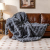 Luxury fuzzy plush rabbit fur bubble blanket in gray draped over a brown sofa, ideal for cozy armchair or bed use.