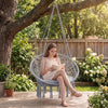 Macrame swing chair with round grey seat cushion, featuring decorative fringes, perfect for indoor or outdoor.