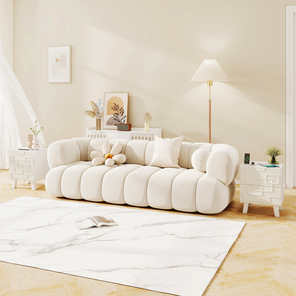 Modern nightstand side table in white with 3D geometric patterns, featuring two drawers for storage beside a couch.