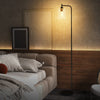 Modern floor lamp with a black finish and clear glass lampshade, featuring a foot switch for easy control in a cozy.