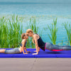 Two people practicing yoga on a navy 4-panel folding gymnastics mat by the water, showcasing comfort and portability.