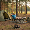 Oversized foldable fishing chair in green with detachable footrest, set up for camping relaxation in the woods.