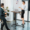 Pneumatic standing desk with adjustable height, anti-fall baffle, and cup holder, shown in a modern office setting.