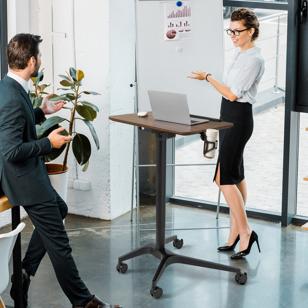 Pneumatic standing desk with adjustable height, anti-fall baffle, and cup holder, shown in a modern office setting.