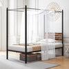 Queen size canopy bed frame in black metal with under bed storage and rustic headboard, styled with sheer curtains.