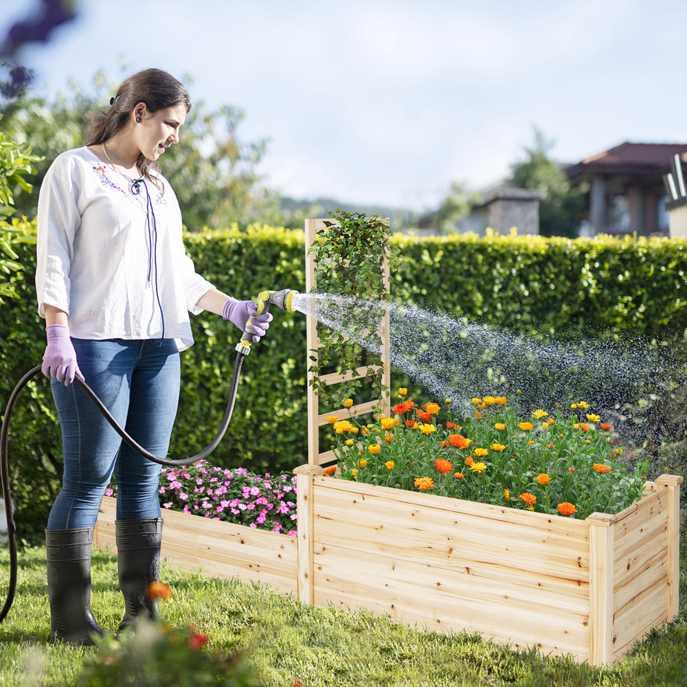 Raised garden bed with trellis in natural fir wood, featuring vibrant flowers and a gardener watering plants.