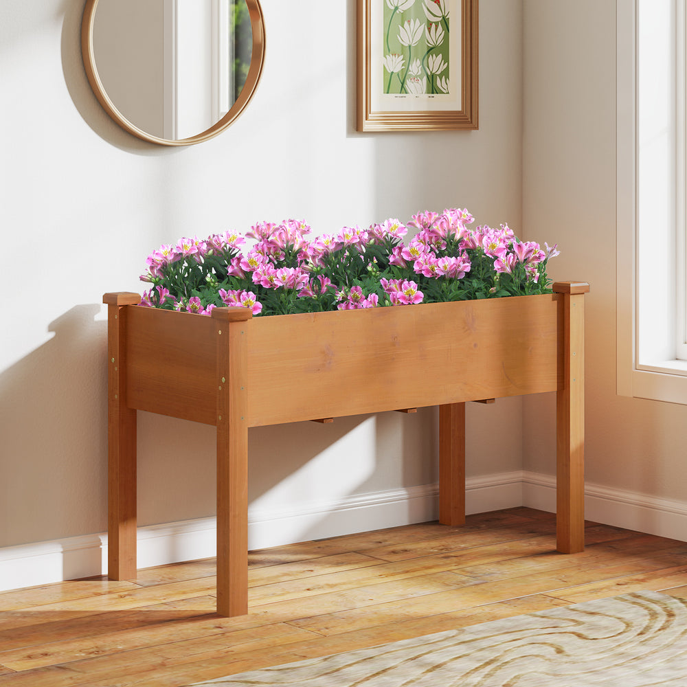 Raised garden bed with legs in brown, featuring drainage holes and filled with pink flowers for indoor or outdoor use.