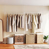 Adjustable floor-to-ceiling tension rod in white, showcasing hanging clothes, ideal for apartments and studios.