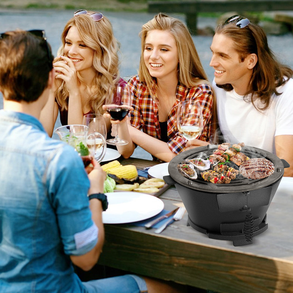 Gathered friends enjoying a meal cooked on a round hibachi grill, highlighting its portable design and outdoor cooking.