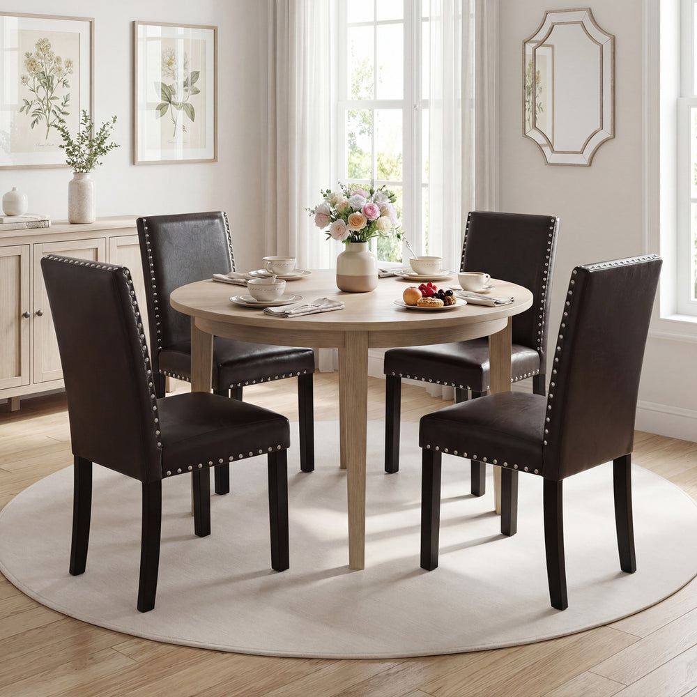 Round dining table set with faux leather upholstered chairs, featuring elegant nailhead accents for modern dining.