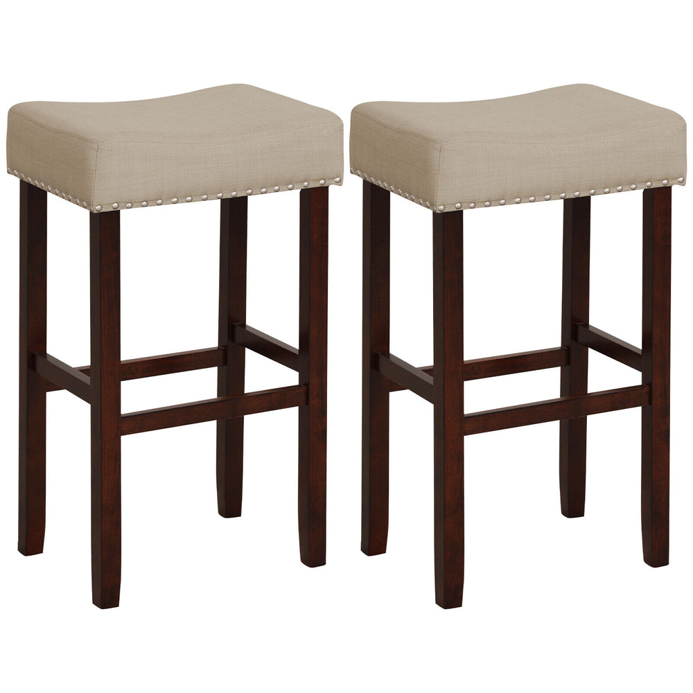 Beige upholstered bar stools with solid rubber wood legs, featuring a curved padded seat and nailhead trim for dining.