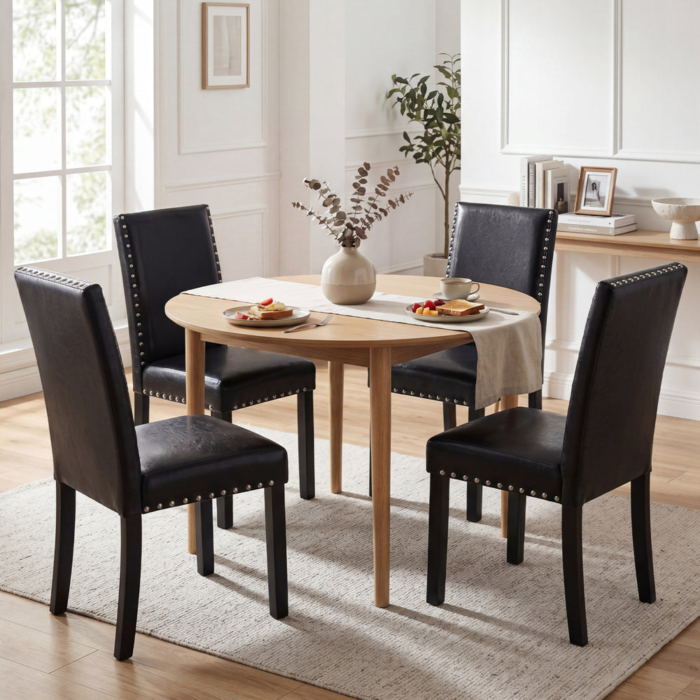 Round dining table set with two black faux leather chairs featuring solid rubber wood legs and elegant nailhead accents.