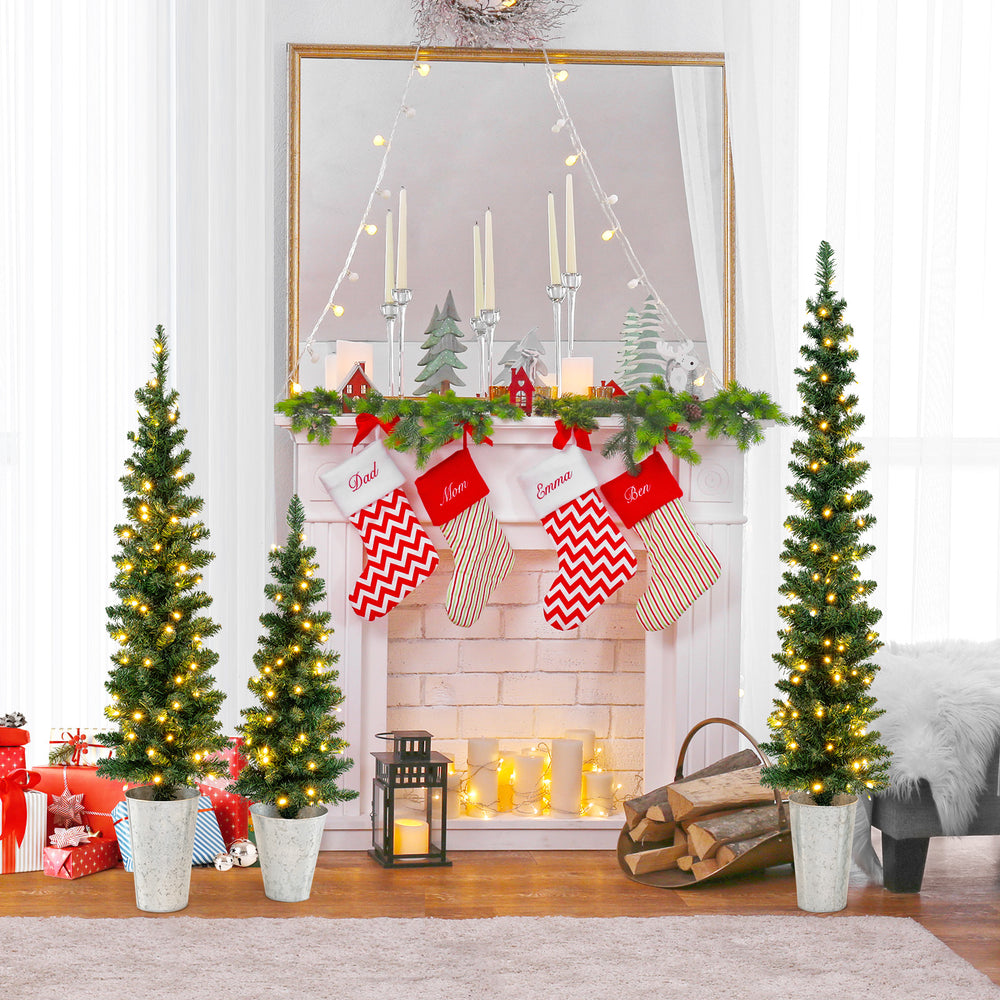 Three pre-lit artificial Christmas trees adorned with warm white LED lights, arranged elegantly by a festive fireplace.