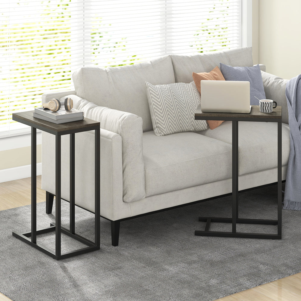 C-shaped side table with oak finish and metal frame, perfect for laptops or tea, placed beside a sofa.