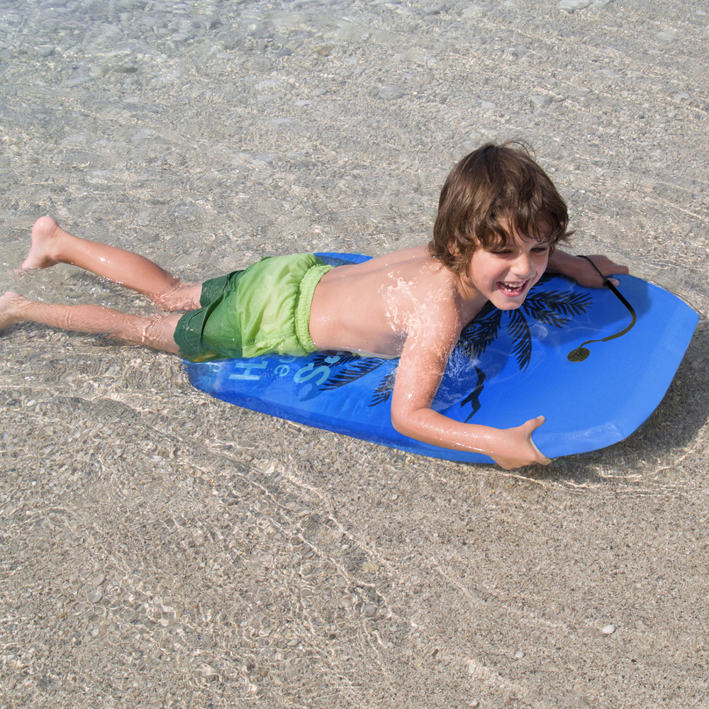Child riding a blue bodyboard with palm design in shallow water, perfect for outdoor surfing adventures.