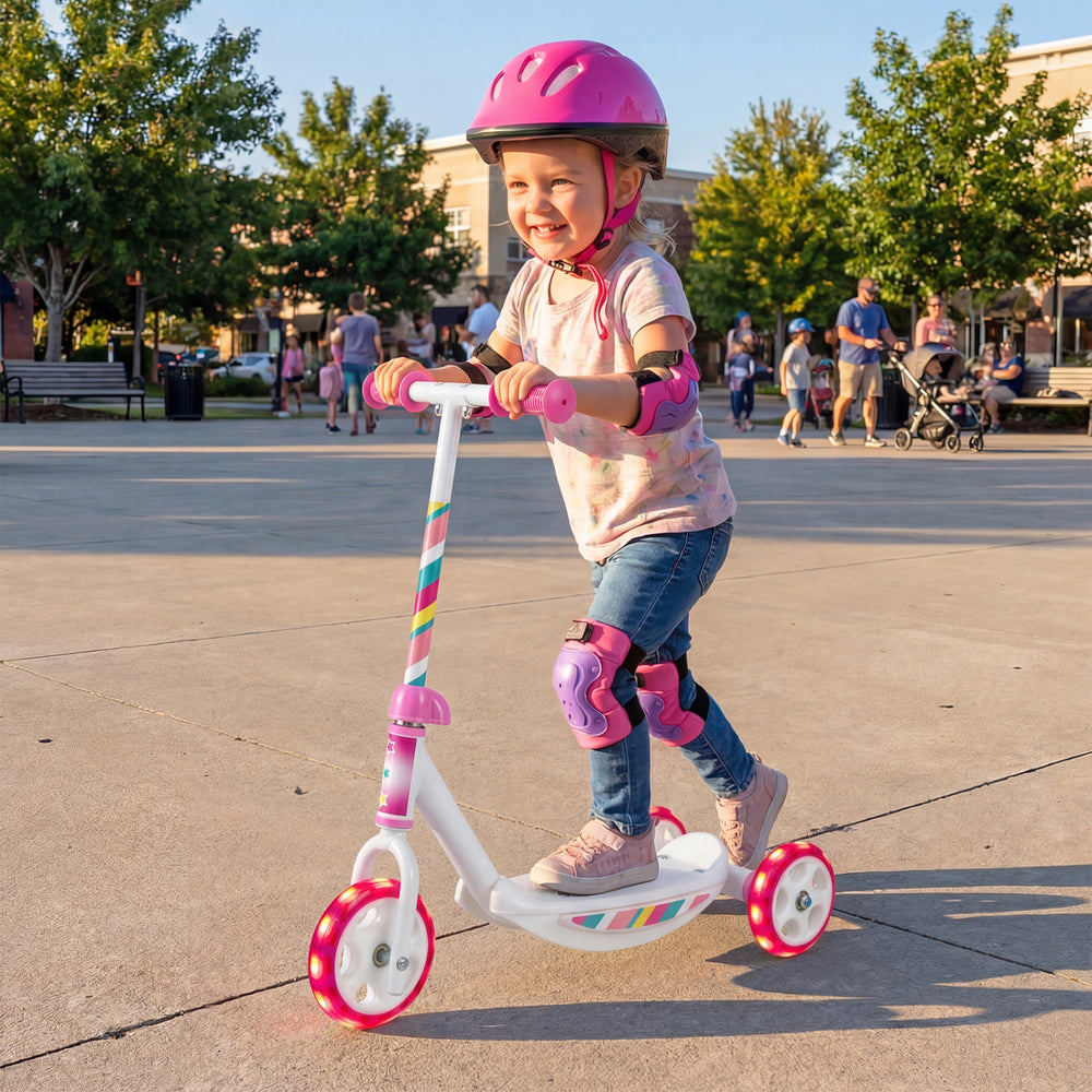 Toddler riding a pink kick scooter with LED light-up wheels and wide anti-slip deck in a park setting.