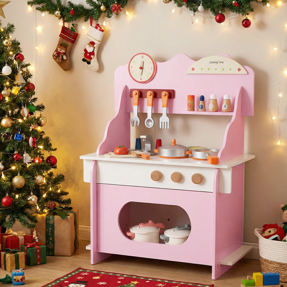 Wooden play kitchen for kids in pink with accessories, clock, and storage, perfect for imaginative pretend play.