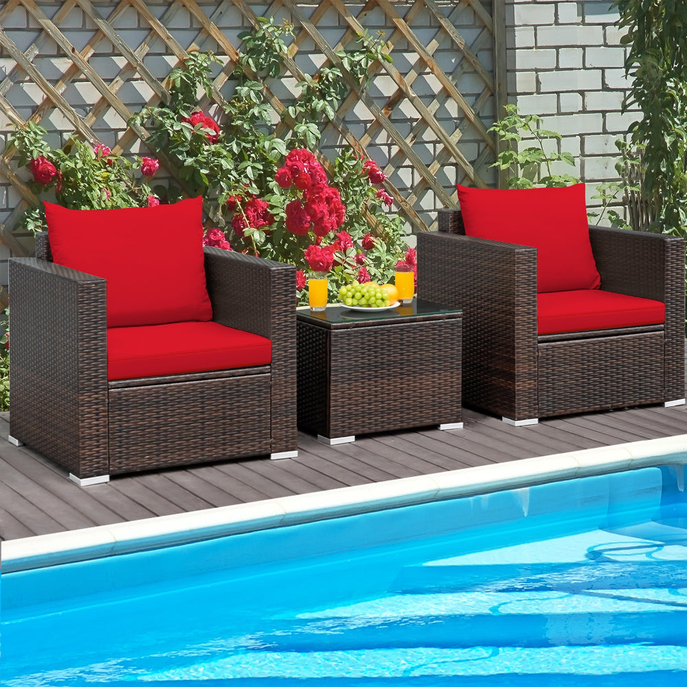 Two red-cushioned rattan chairs with a glass-top table by the pool, perfect for outdoor relaxation.