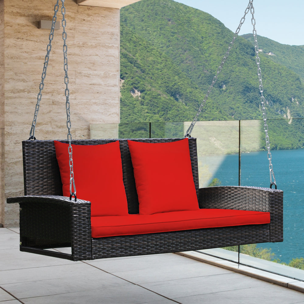 Rattan porch swing for two with red cushions, featuring sturdy steel chains for secure outdoor relaxation.