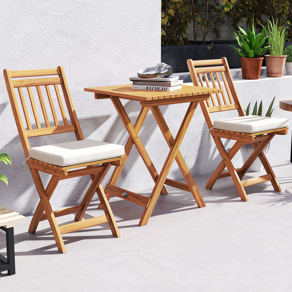 Outdoor wood bistro set featuring a folding table and two chairs with soft seat cushions, perfect for backyard.
