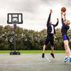 Two players engaging in a basketball game with a portable hoop featuring a shatterproof backboard and adjustable height.