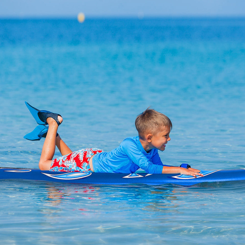 Child lying on a 6-foot surfboard in the ocean, featuring a durable foam top and removable fins for easy transport.