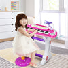 Child playing the pink 37 key electronic keyboard piano with detachable microphone and stool in a bright room.