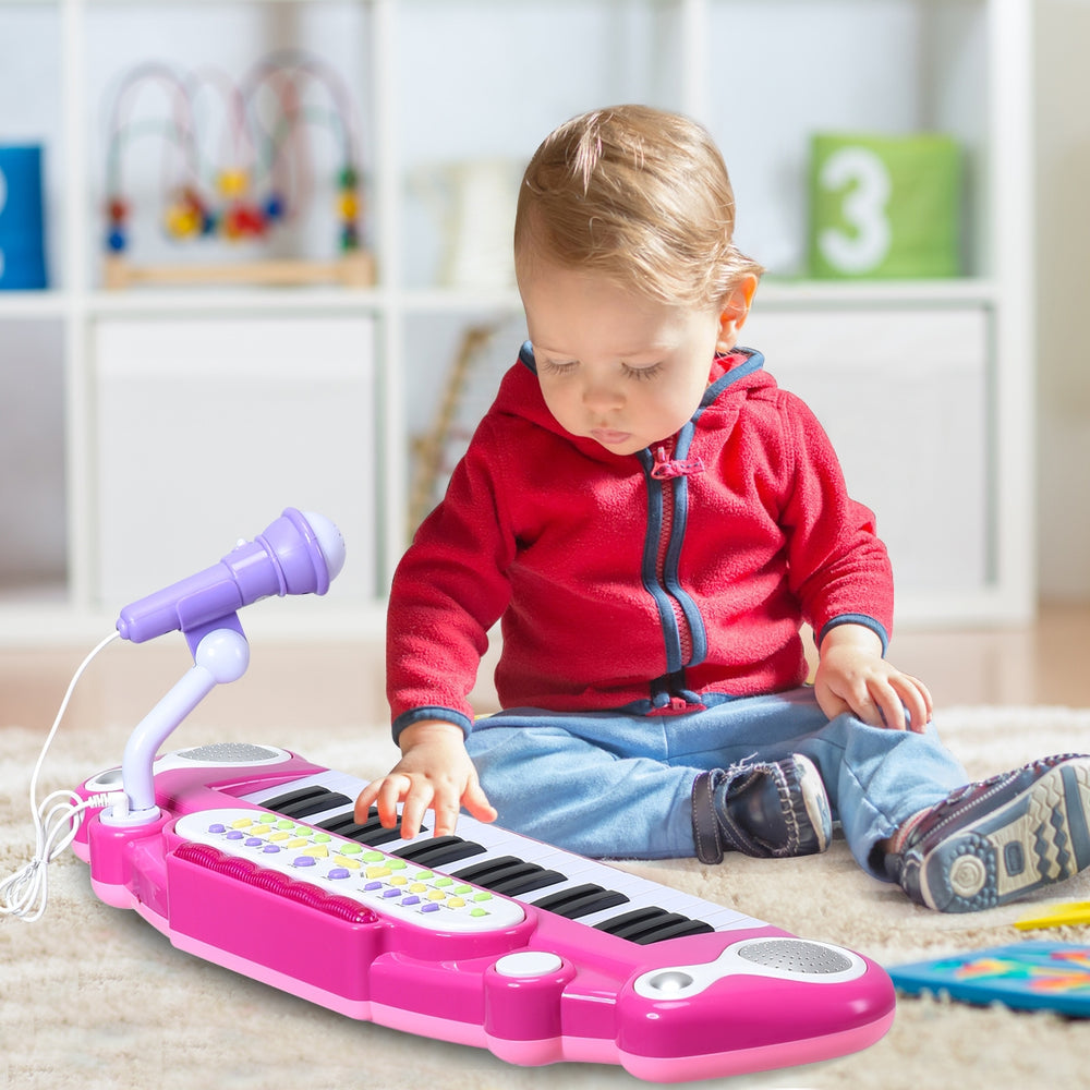 Child playing with a pink 37-key electronic keyboard piano toy, featuring a microphone and sturdy design for safe fun.