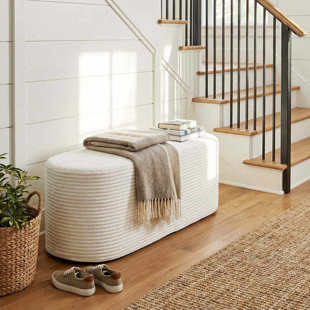 Upholstered beige ottoman bench with oval shape and corduroy surface, perfect for entryway or living room use.
