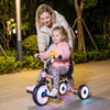 Toddler riding a foldable tricycle with glowing wheels, featuring a basket and duck bell, perfect for outdoor fun.